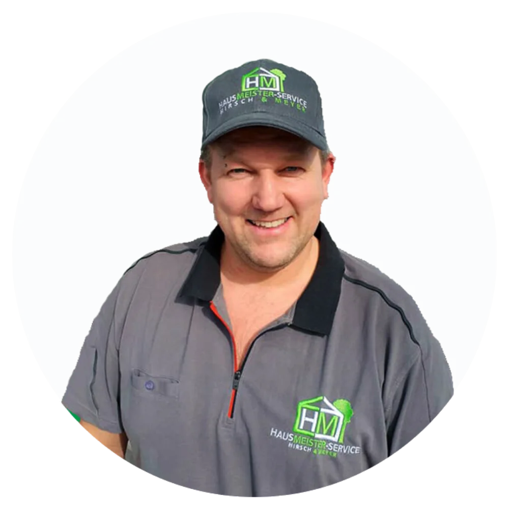 Mitarbeiter von Hausmeisterservice Hirsch & Meyer mit Logo-Shirt und -Kappe, lächelnd vor transparentem Hintergrund für Web- oder Printverwendung.