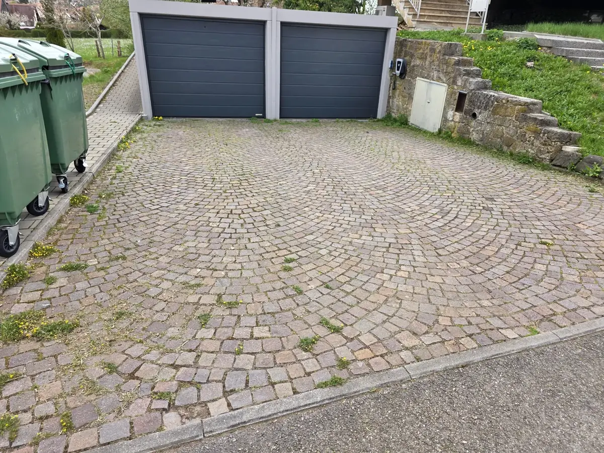 Verschmutzte, bewachsene Pflasterfläche vor der Garage